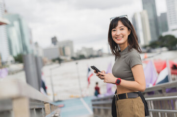 Happy young southeast asian woman teenager blogger and world travel explorer using smartphone...