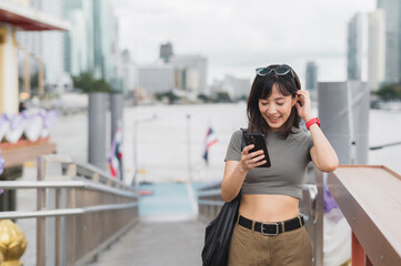 Young southeast asian woman teenager blogger using smartphone searching tourism guide for world...