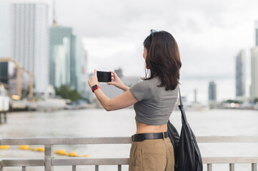 Solo southeast asian woman teenager blogger take photo with smartphone and wait for boat. An express world travel explorer tourism concept for local cultural experience Chao Phraya river Bangkok