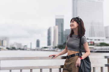 Happy solo Southeast Asian woman teenager blogger world travel tourism. An explorer enjoys local cultural experience Bangkok Thailand. Wait for express boat Chao Phraya River. travel concept Asia