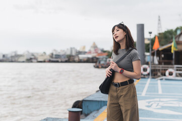 Contemplative solo southeast asian woman teenager blogger and world travel explorer wait for express boat. Local cultural experience asia tourism concept by Chao Phraya river Bangkok Thailand