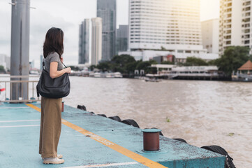 Solo southeast asian woman teenager blogger and world travel explorer wait for an express boat at Chao Phraya River Bangkok for local cultural experience an asia tourism concept in Thailand