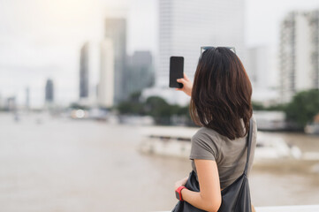 Solo southeast asian woman teenager blogger world travel explorer take photo with smartphone. Express local cultural experience wait for boat chao phraya river bangkok thailand. Asia tourism