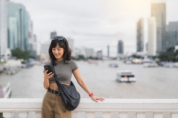 Happy young southeast asian woman teenager blogger and world travel explorer using smartphone searching tourism guide Chao Phraya river Bangkok Asia. local cultural experience tourism concept