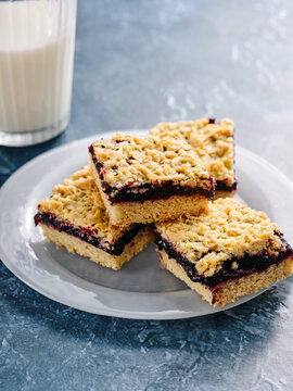 Four jam shortbread bars are arranged neatly on a plate, showcasing their golden crust and rich berry filling. A glass of milk sits nearby, making it a perfect dessert pairing