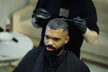 Barber coloring hair of african american man in barbershop 