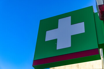 A white cross on a green background on a luminous banner hanging on the facade of a building, a...