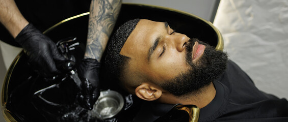 Web banner of tattooed barber holding faucet near sink and african american client in barbershop