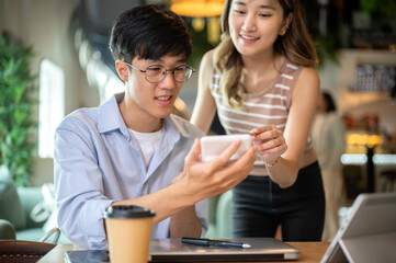 Asian woman standing and bending over wooden table helping a man with calculator in cafe or canteen.