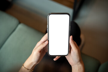Close up of a woman's hands holding blank screen smartphone while sitting cross legs on green sofa.