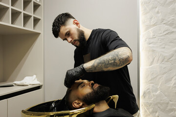 Barber washing head of bearded african american client in barbershop