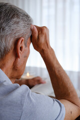 Senior man reading a book at home with thoughtful expression, over the shoulder view