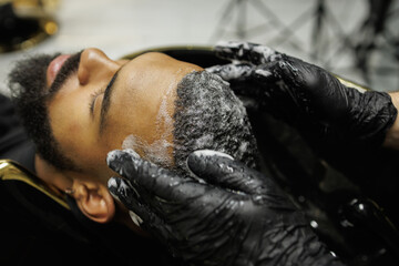 Close up of barber in latex gloves washing hair of african american man