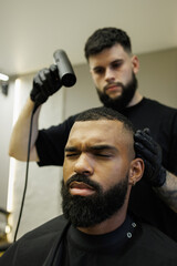 Blurred barber holding hairdryer near african american client in barbershop