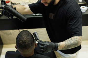 Top view of tattooed barber drying hair of african american client in barbershop