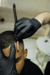 Close up of barber in latex gloves shaving forehead of client african american client 