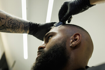 Low angle view of tattooed barber shaving forehead of african american client