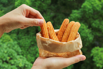 Bag of Delectable Freshly Fried Churros against Blurry Green Foliage Background
