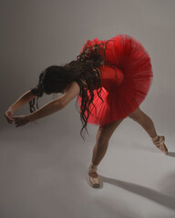 Brunette ballerina in red tutu and pointe shoes, standing in classical dance poses with back facing...
