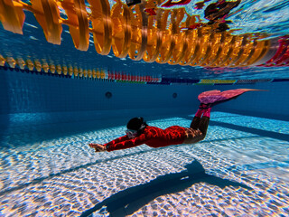 Young woman with mermaid tail swims and dives under sunlit deep water