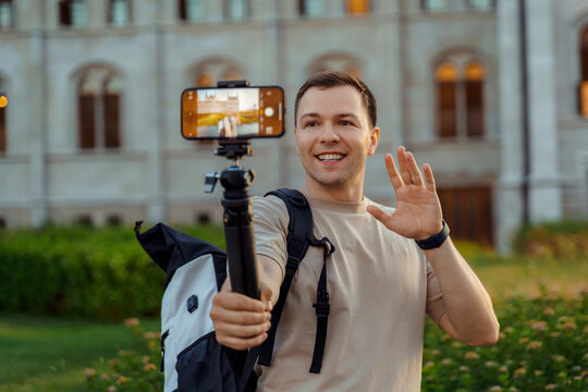 Happy male travel blogger vlogging with smartphone and waving to audience