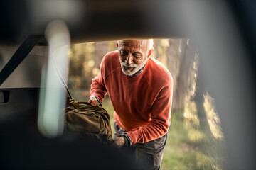 Senior Man Unpacking Camping Gear from Vehicle in Scenic Outdoors
