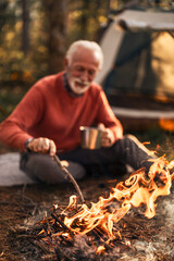 Elderly Camper Enjoying Fire in Forest Campsite