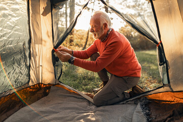 Senior Camper Organizing Tent Interior in Forest at Sunset