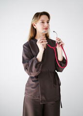 Portrait of a smiling young female doctor in a dark uniform holding a pink stethoscope, looking away, isolated on white background.