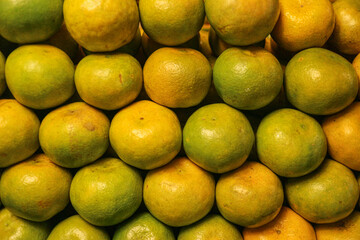 Wide angle view of fresh Thai honey tangerines arranged in a row, golden yellow mixed with green peel, sweet tangy flavor and natural textured skin, popular local street fruit.