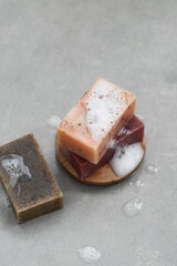 Three natural organic handmade soap bars with white foam on a gray concrete background