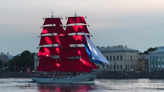 Famous ship with scarlet red sails down river. Beautiful brig cuts through blue water during white nights. Graduates' holiday. Pretty amazing boat. Russian flag, Russia. Traditional Sailboat tour.