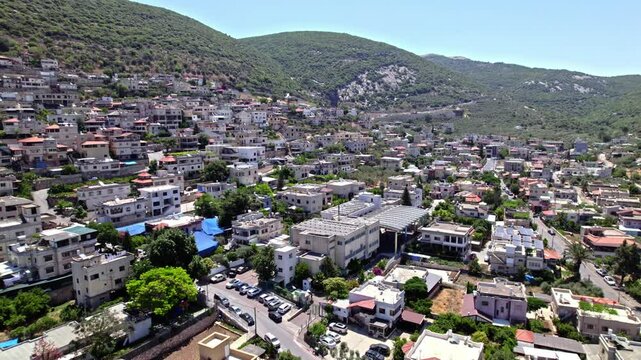 Aerial view of the Druze town of Peki'in in northern Israel, surrounded by lush green mountains under a clear summer sky.