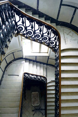 Spiral staircase in historic interior with marble steps and wrought iron railing. Old European building architecture with vintage style. Concept of cinematic mysterious ambiance, history and elegance