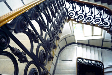 Beautiful curves and visual balance: architectural top-down view of spiral stairway with iron railing and marble steps. Life in an old European house: the beauty of the interior in a public space.