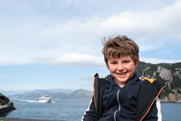 Fototapeta premium Smiling happy boy looking at camera with sea bay and boat in background.Text space.