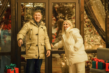 Cheerful couple enjoys holiday shopping while surrounded by Christmas decorations and gifts. Festive Christmas market, gifts, discounts, shopping, sale, winter holidays concept.