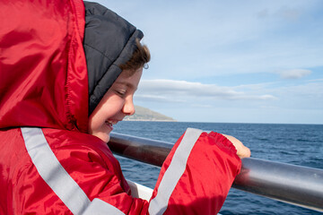 Smiling 5-year-old boy holding boat railing during sea trip in Italy