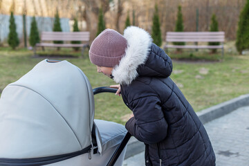 Curious girl looking into baby stroller outdoors