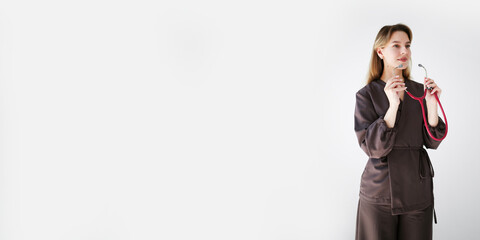 Wide banner with a smiling young female doctor in dark uniform holding a pink stethoscope, looking away, isolated on white background with copy space.