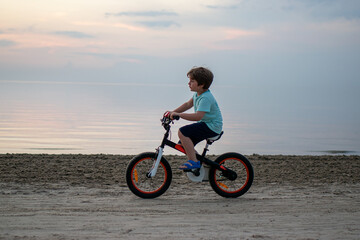 Boy learning to ride a bicycle on a sandy beach at summer sunset