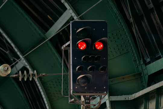 A railroad signal with two red lights indicating 'stop' for the train. A dark scene at Hagen main station in Germany, with a green steel roof construction in the background. Train traffic image
