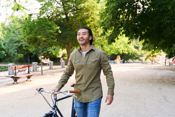 Young man walking with his bicycle in a city park