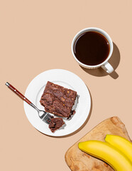 Сhocolate banana brownie on a plate on a beige background with a cup of coffee and fresh fruits.