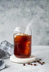 Cold brew coffee in a glass with ice on a marble stand on a light concrete background with coffee beans