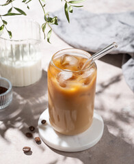 Ice latte coffee in a glass with milk on a light background with coffee beans and morning shadows.