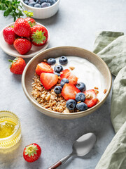 Natural yogurt with granola, blueberry and strawberry in a bowl on a light background