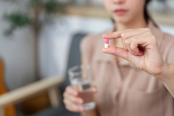 Medication Management. Woman preparing to take a capsule with a glass of water.