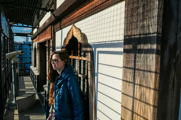 Female tourist in sunglasses enjoys sun on the observation deck of Hiroshima Castle, Japan. Strong light casts a grid of shadows. Historic wooden architecture, creating unique, memorable travel moment