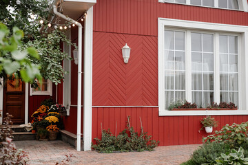 Part of red village house with big window, potted plants and blooming tree with no people around